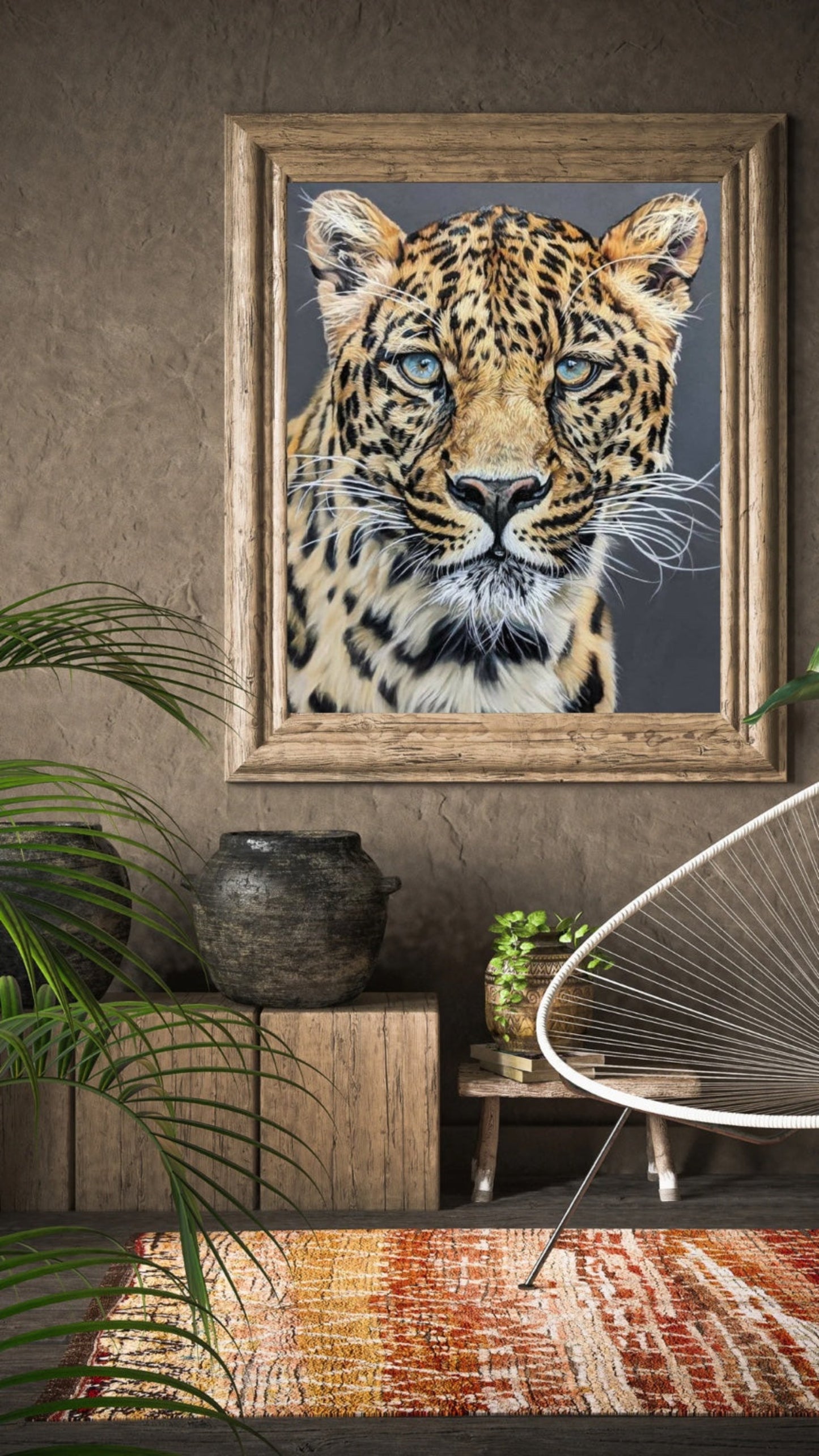 Framed picture of a leopard on a wall with a chair and plants in the foreground